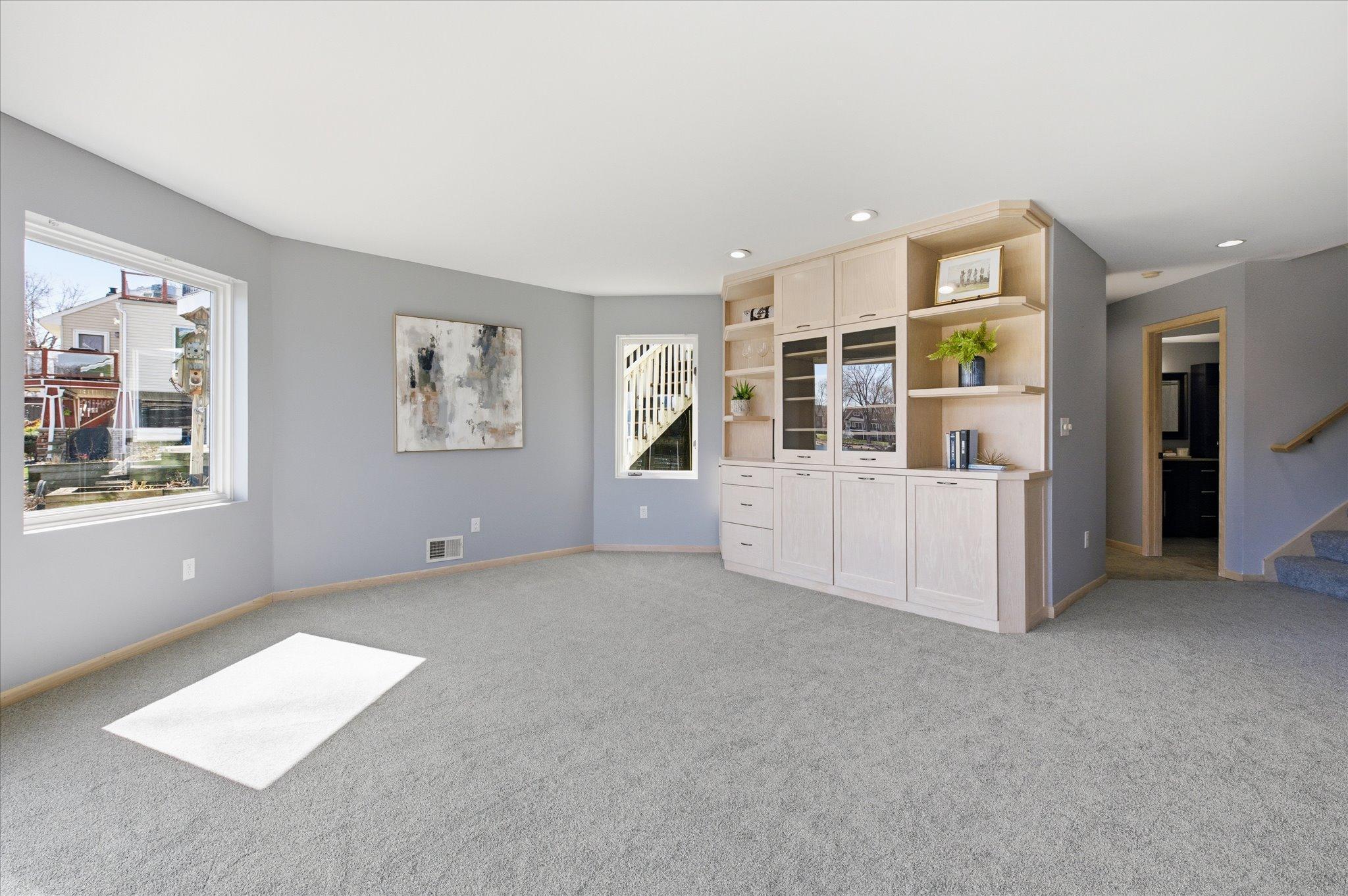 Spacious lower-level family room with plush carpet, recessed lighting, and custom built-in cabinetry for storage and display.
