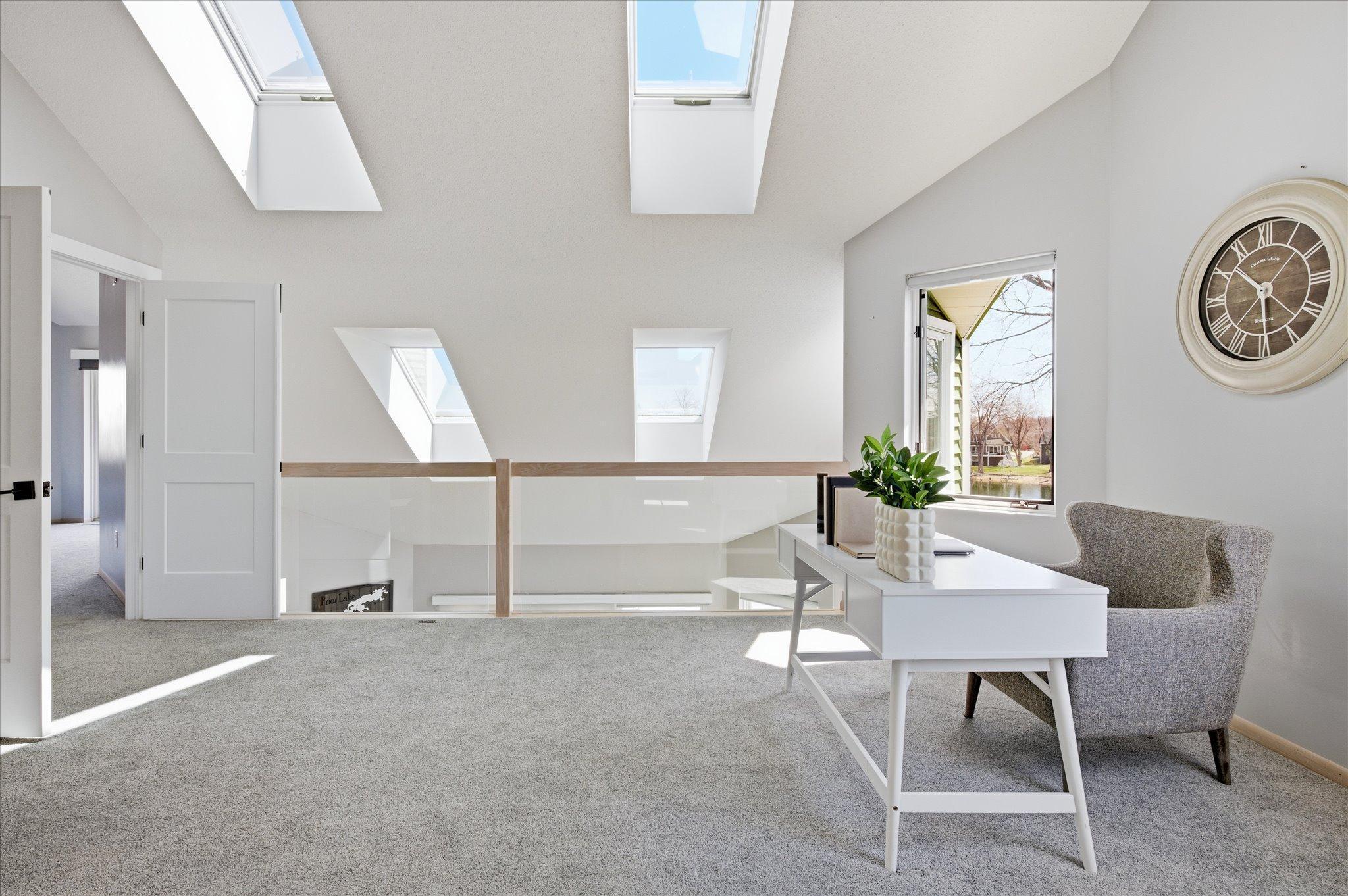 Loft overlooking the main level with skylights and modern glass railing, enhancing openness and light.