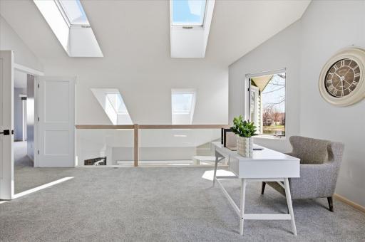 Loft overlooking the main level with skylights and modern glass railing, enhancing openness and light.
