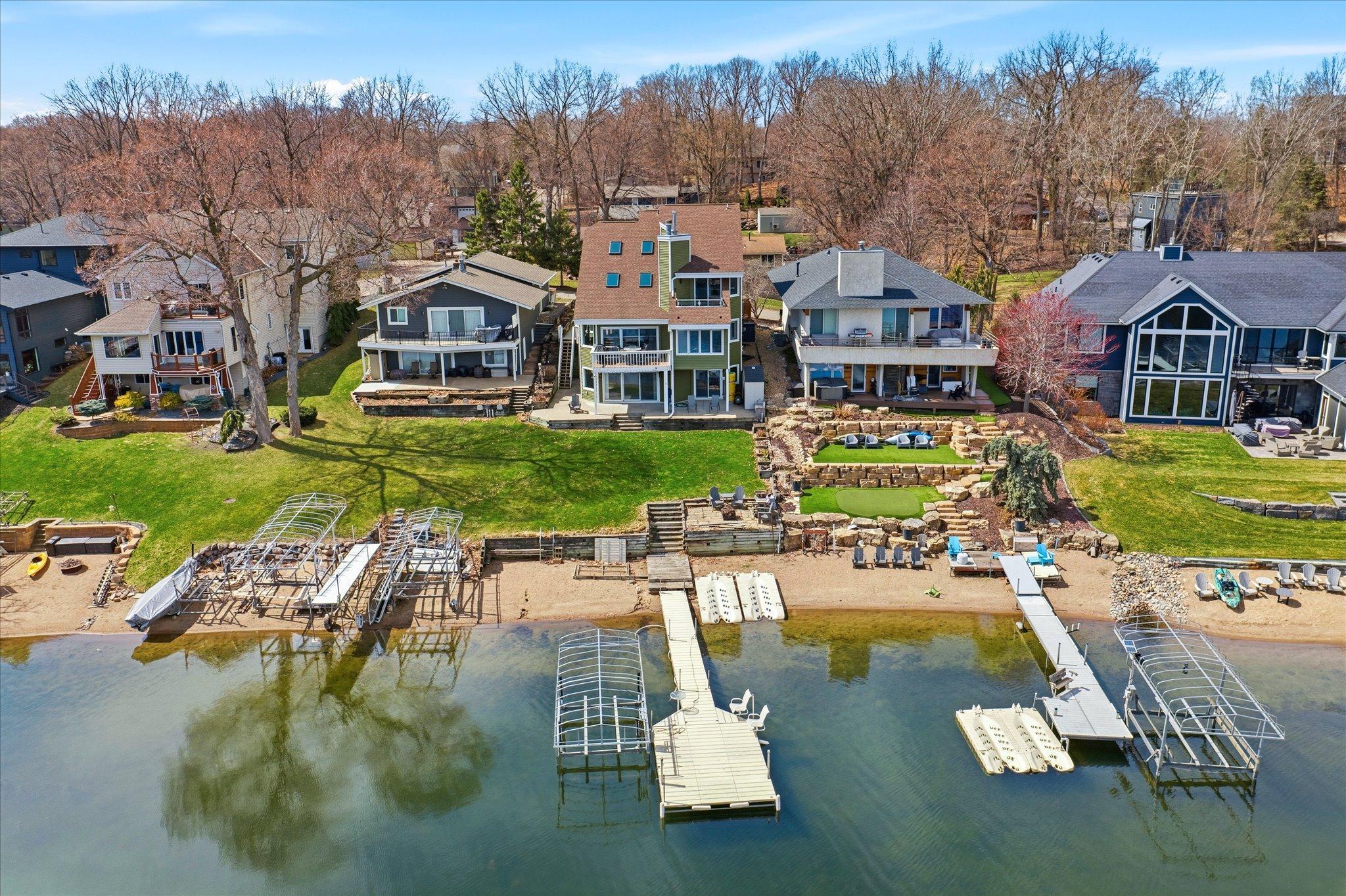 Rear aerial showcasing tiered outdoor living spaces leading to the shoreline.