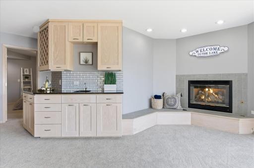 Lower-level entertaining area with built-in wet bar, cabinetry, and tile-surround gas fireplace.