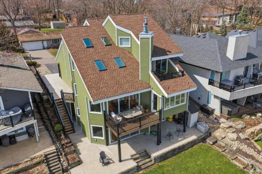Aerial rear exterior showcasing multi-level home, expansive deck, and walkout patio with virtually staged black iron railings; seller offering full allowance for deck/railing replacement.