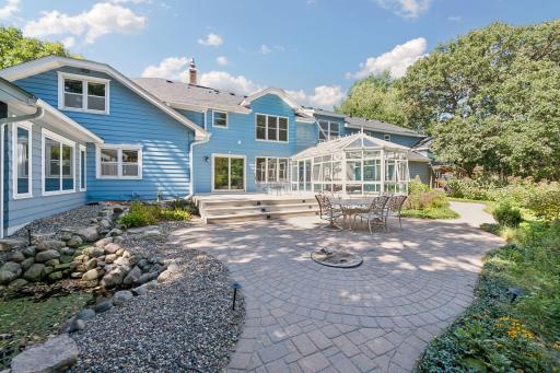 A stunning paver patio surrounded by professional landscaping and mature trees creates a true backyard oasis.