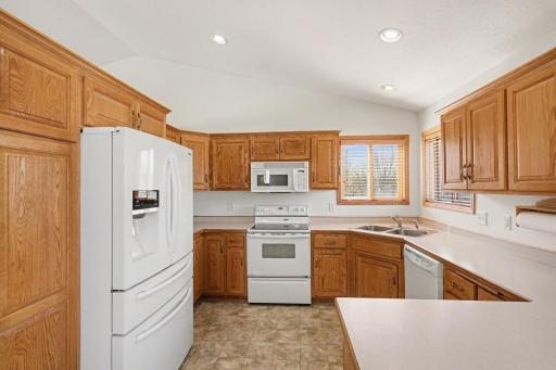 The kitchen features: a generous amount of cabinetry & countertops, an updated refrigerator (2021), a vaulted ceiling with recessed lights, and a corner sink with south & west-facing windows.