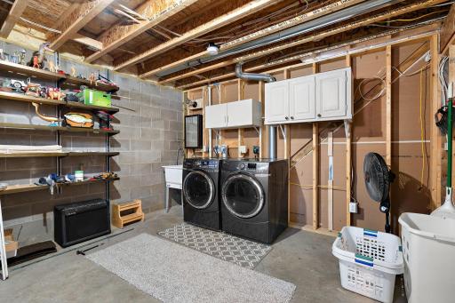 The lower level has an unfinished storage space and laundry room area with a laundry sink to the left of the washer and dryer.