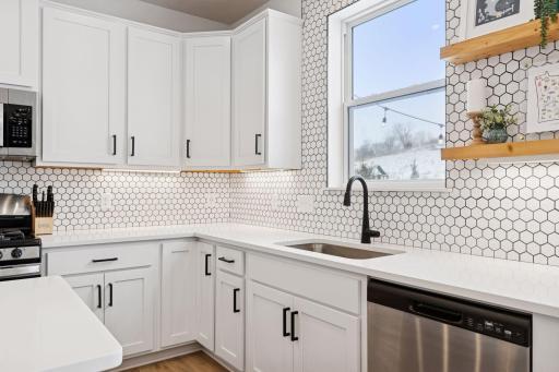 Hardwired under cabinet lighting, recently finished tile backsplash, large under mount kitchen sink, and floating shelving next to window.
