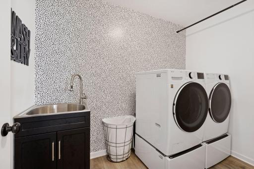 Recently finished laundry room with accent wallpaper, new slop sink, and hanging for clothes.