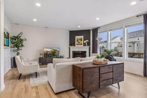 Bright, open living space anchored by a fireplace and a wall of windows.