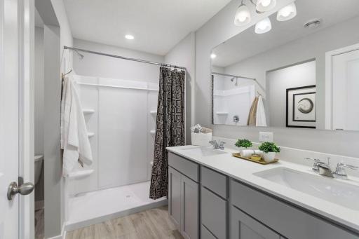 A peak inside the bathroom off the Primary Suite. Notice the extra high cabinets and double-bowl Quartz covered vanity with loads of storage! Photo is of model home. Colors and options may vary. Ask Sales Agent for details.