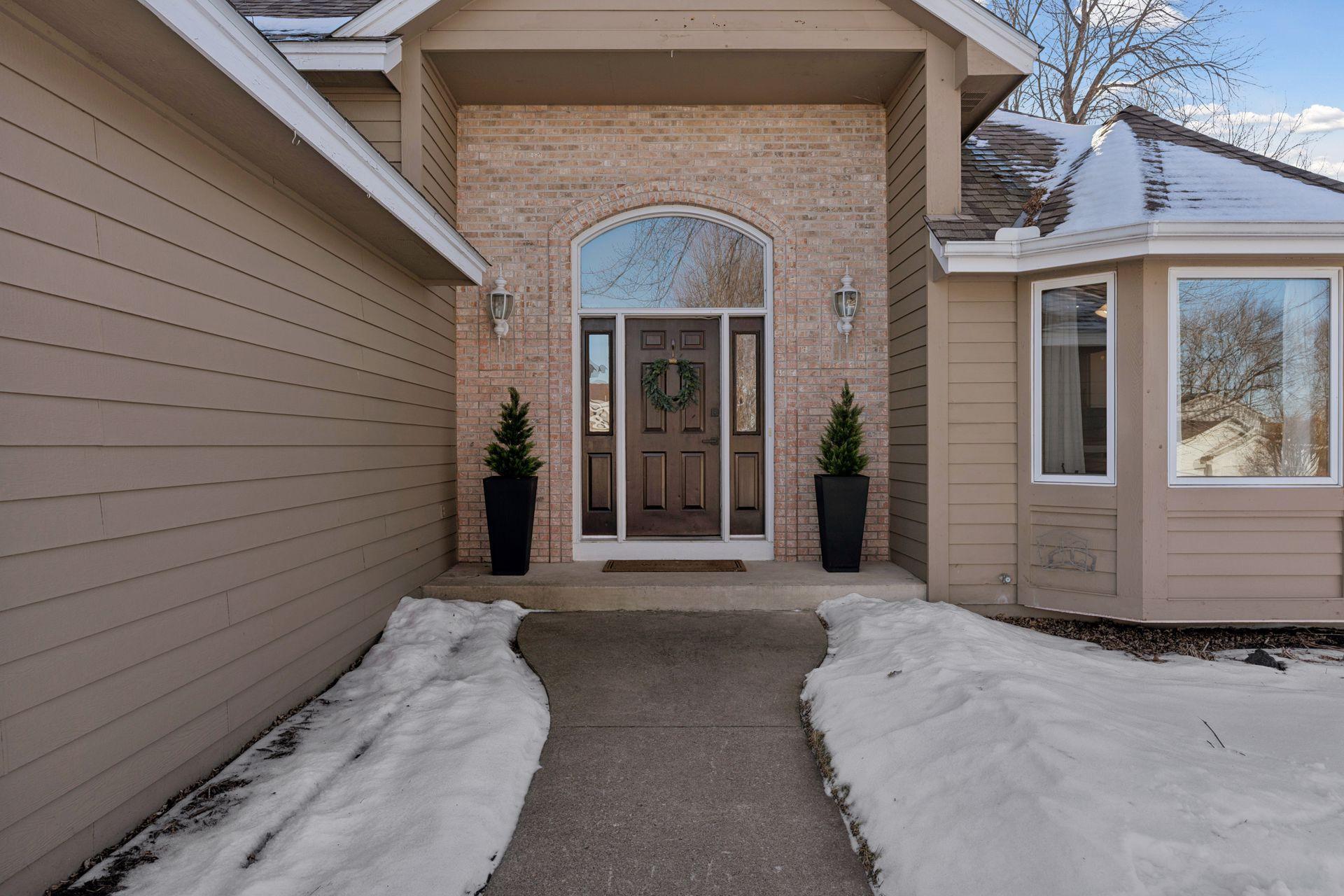 Exterior view of the covered grand two story entry highlighted w/ brick and an oversized front entry door w/ large transom window.