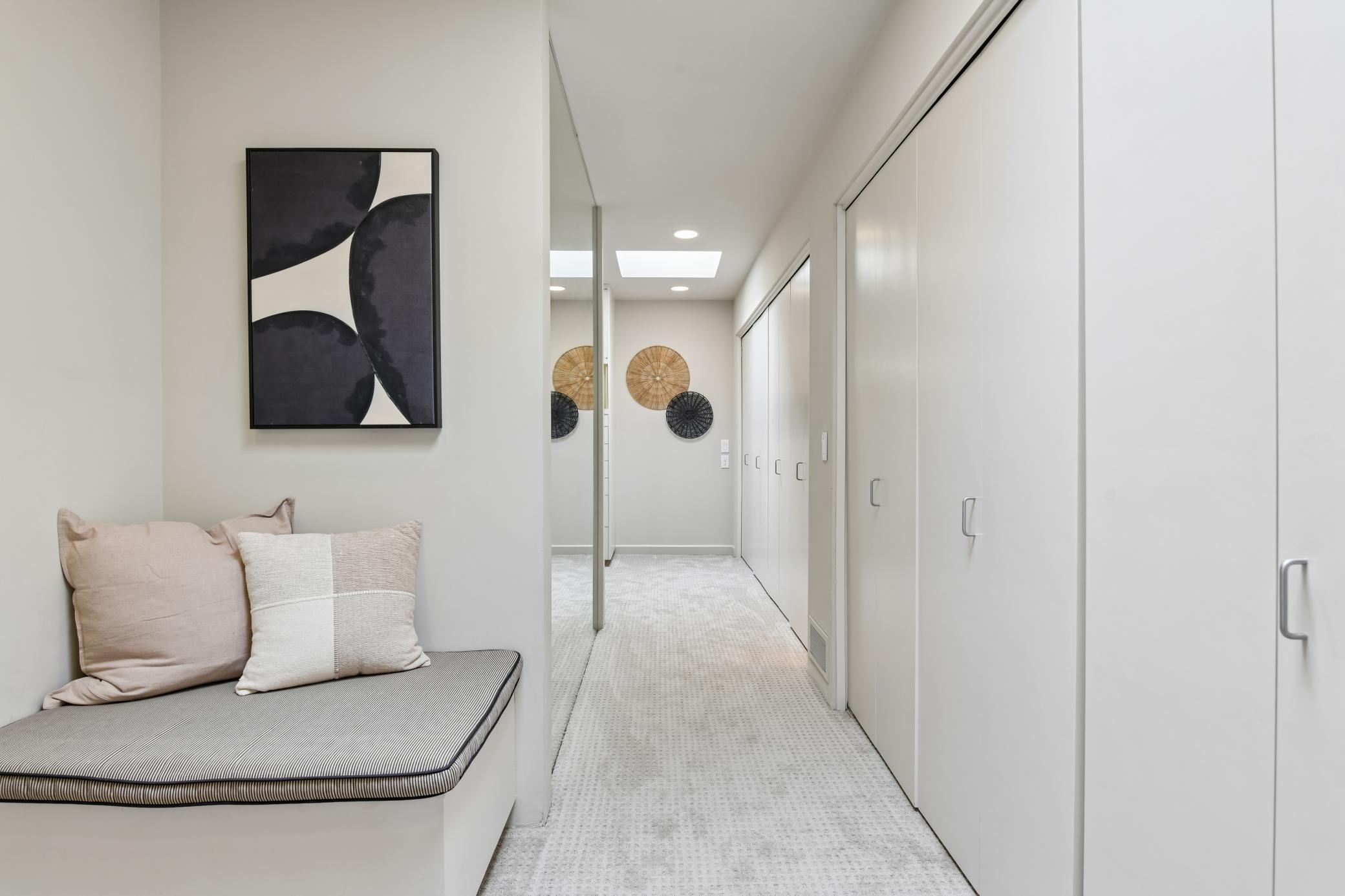 The walk-through closet features a full wall of expansive hanging closet space, as well as two built-in dressers, benches with storage and an oversized full length mirrror.