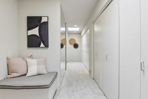 The walk-through closet features a full wall of expansive hanging closet space, as well as two built-in dressers, benches with storage and an oversized full length mirrror.