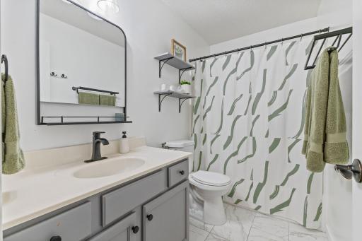 The main floor bathroom, one of two full baths, features a modern look with tile floors, painted cabinetry, and updates mirror, faucet, light fixture and shelving.
