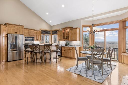 The kitchen features custom cabinetry, stainless appliances, granite countertops and gleaming wood floors accented by panoramic views. Cozy kitchen dining area with gas fireplace walks out to maintenance free deck.