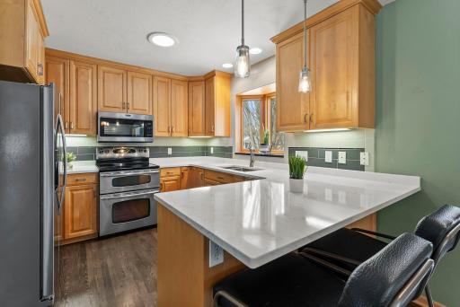 The bright kitchen is thoughtfully designed with a tile backsplash, stainless steel appliances, abundant cabinetry, a large pantry, and breakfast bar seating at the peninsula. A charming bay window brings in additional natural light and character.