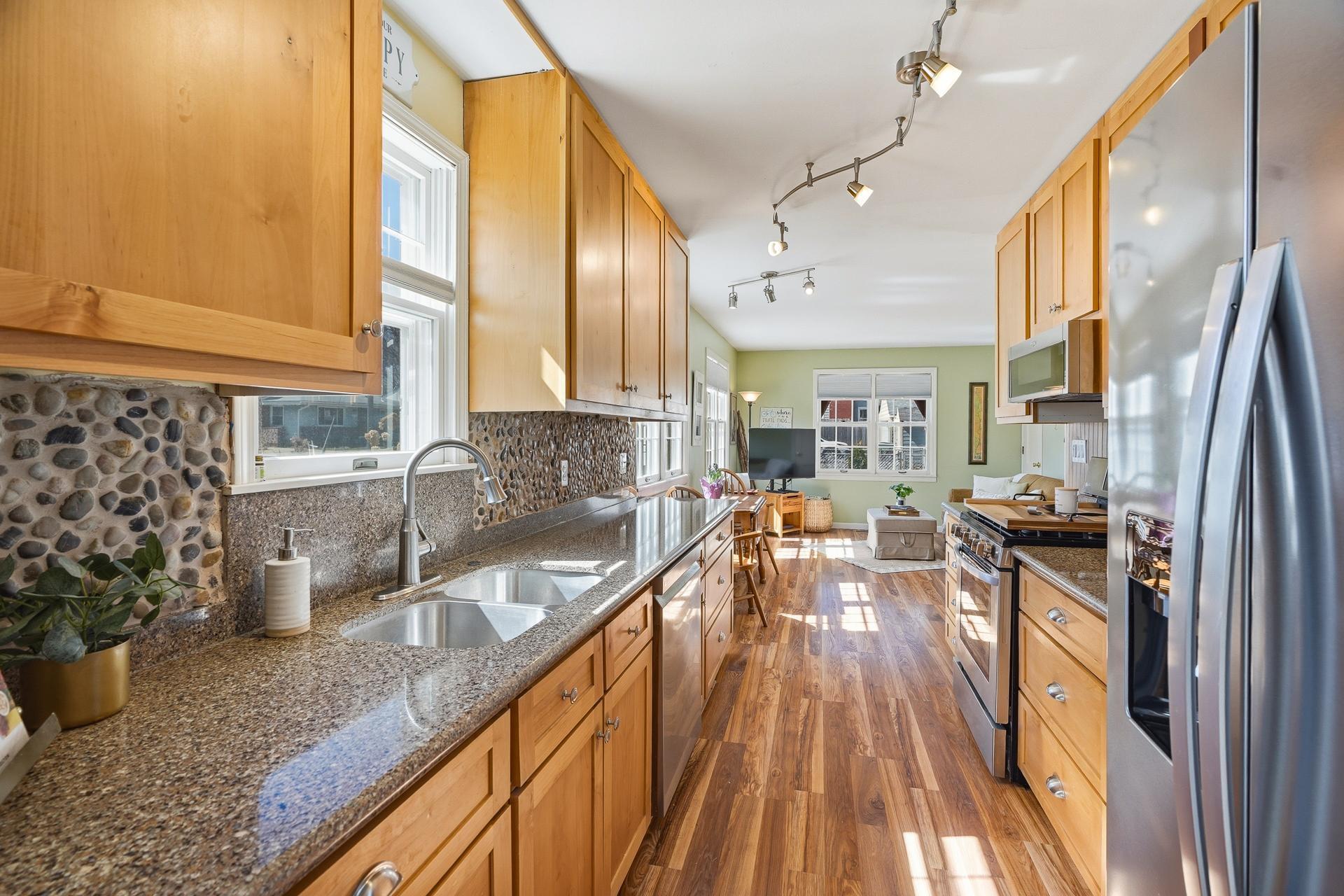 The renovated kitchen features new cabinetry with soft close drawers, granite countertop, pebble tile backsplash, stainless appliances and a window over the sink.