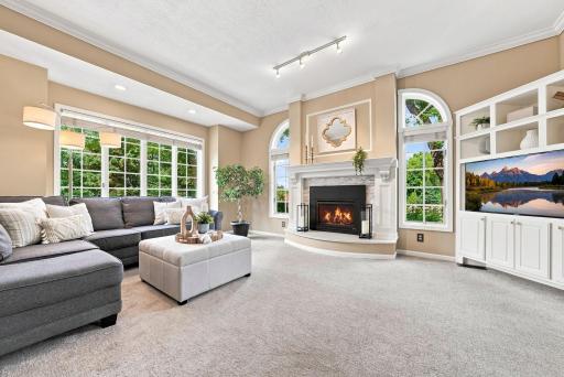 A wider view of the living room reveals soaring vaulted ceilings and an elegant marble fireplace surround and arched windows that flood the space with natural light..