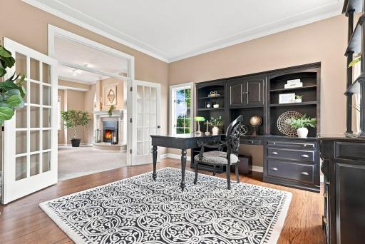 A private main floor office enclosed with French doors, featuring built-in bookshelves, rich hardwood floors, and a window overlooking the front grounds, the ideal work-from-home retreat.
