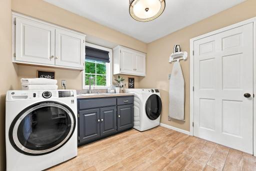 A spacious laundry room with side-by-side washer and dryer, custom native cabinetry, and a bright window overlooking the backyard.