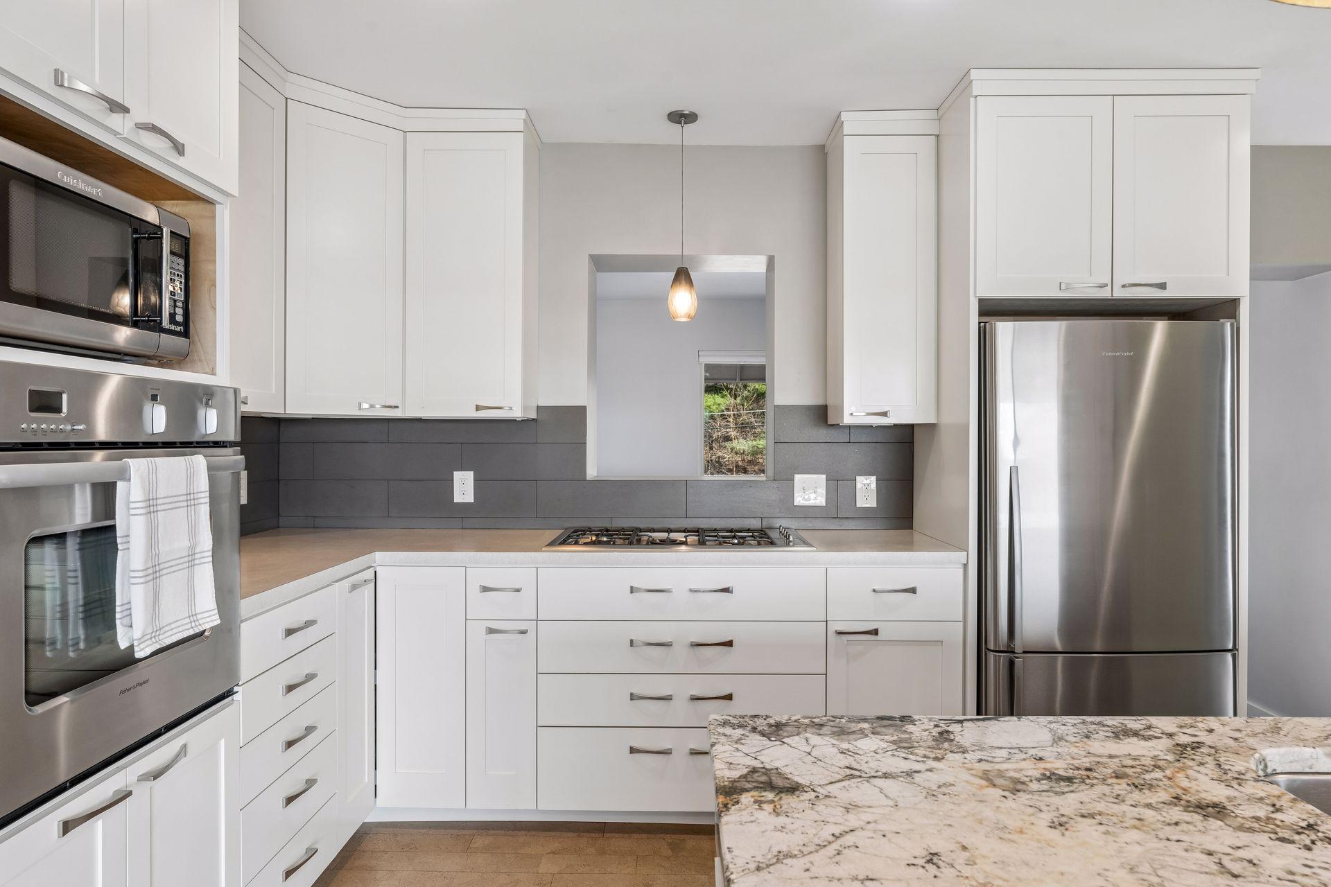 Fisher & Paykel gas cooktop and wall oven, birch cabinetry, tile backsplash and cutout window into dining room.