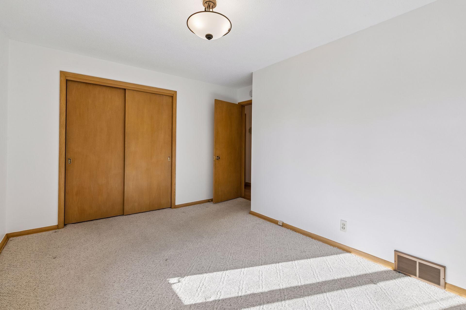 Bright second bedroom on the main floor with carpeted floors, overhead light, and generous double closet space.