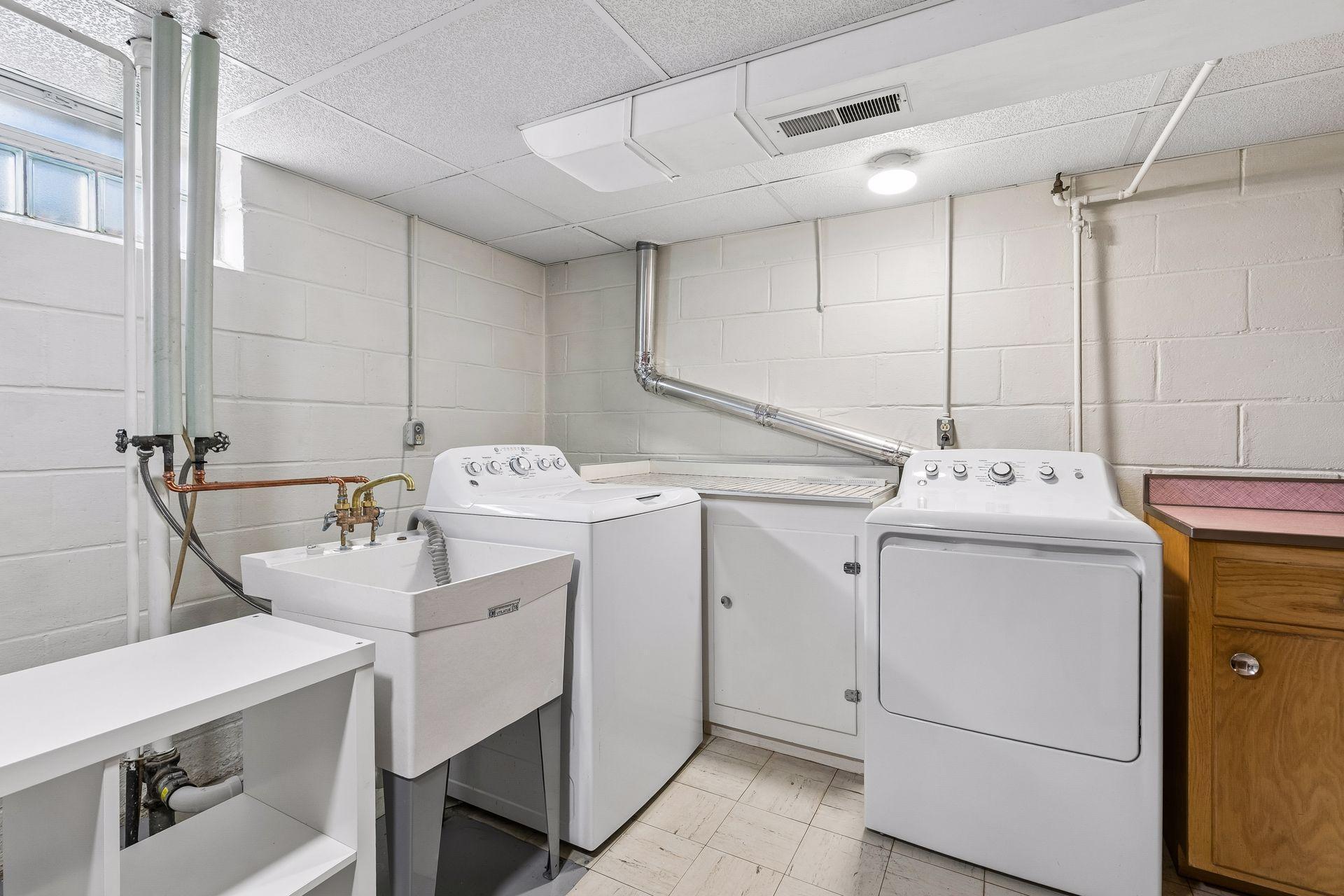 Well equipped laundry and mechanical room with tile flooring, a utility sink, and bright overhead lighting.