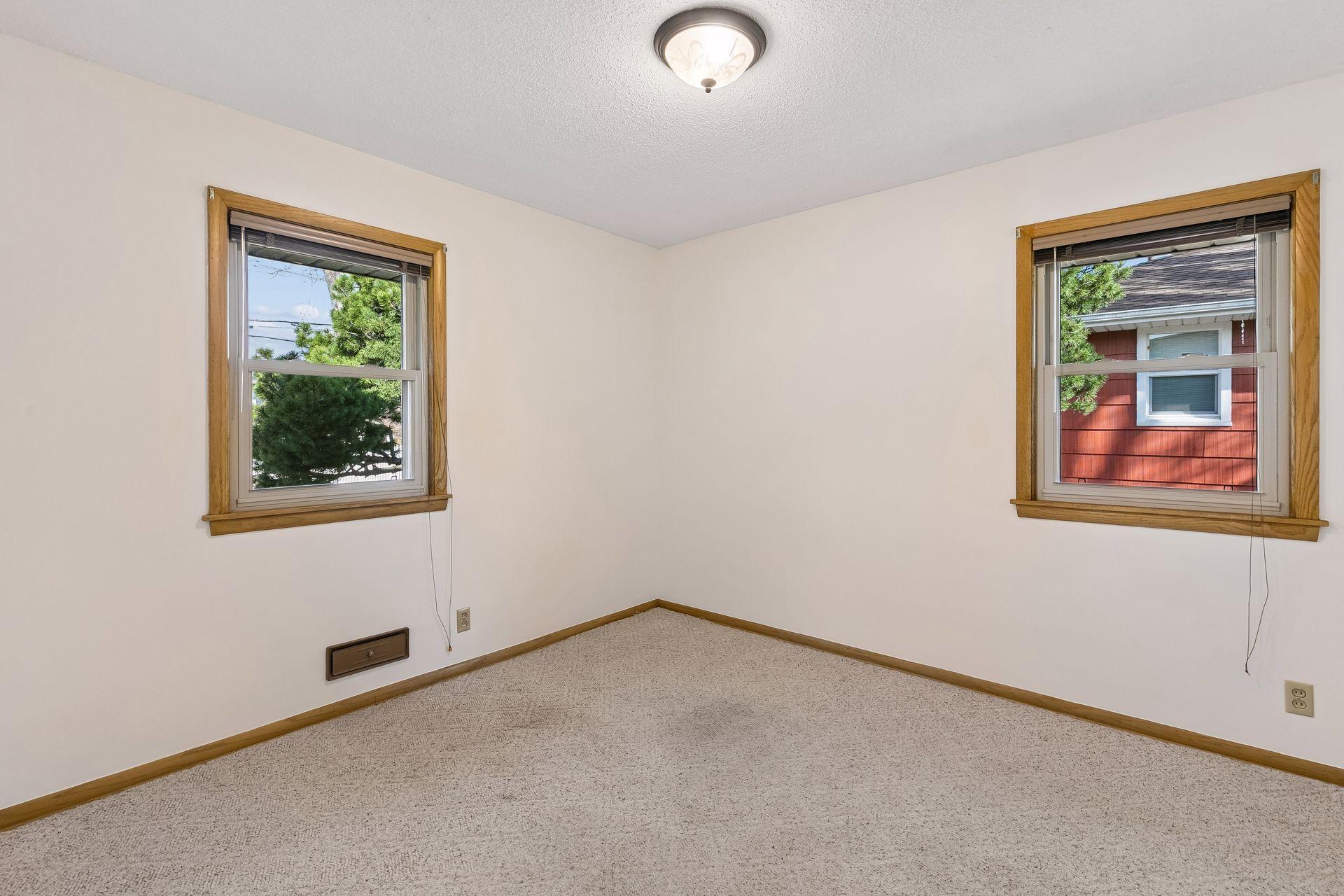 Cozy main floor bedroom featuring carpet, overhead lighting, and two bright windows.