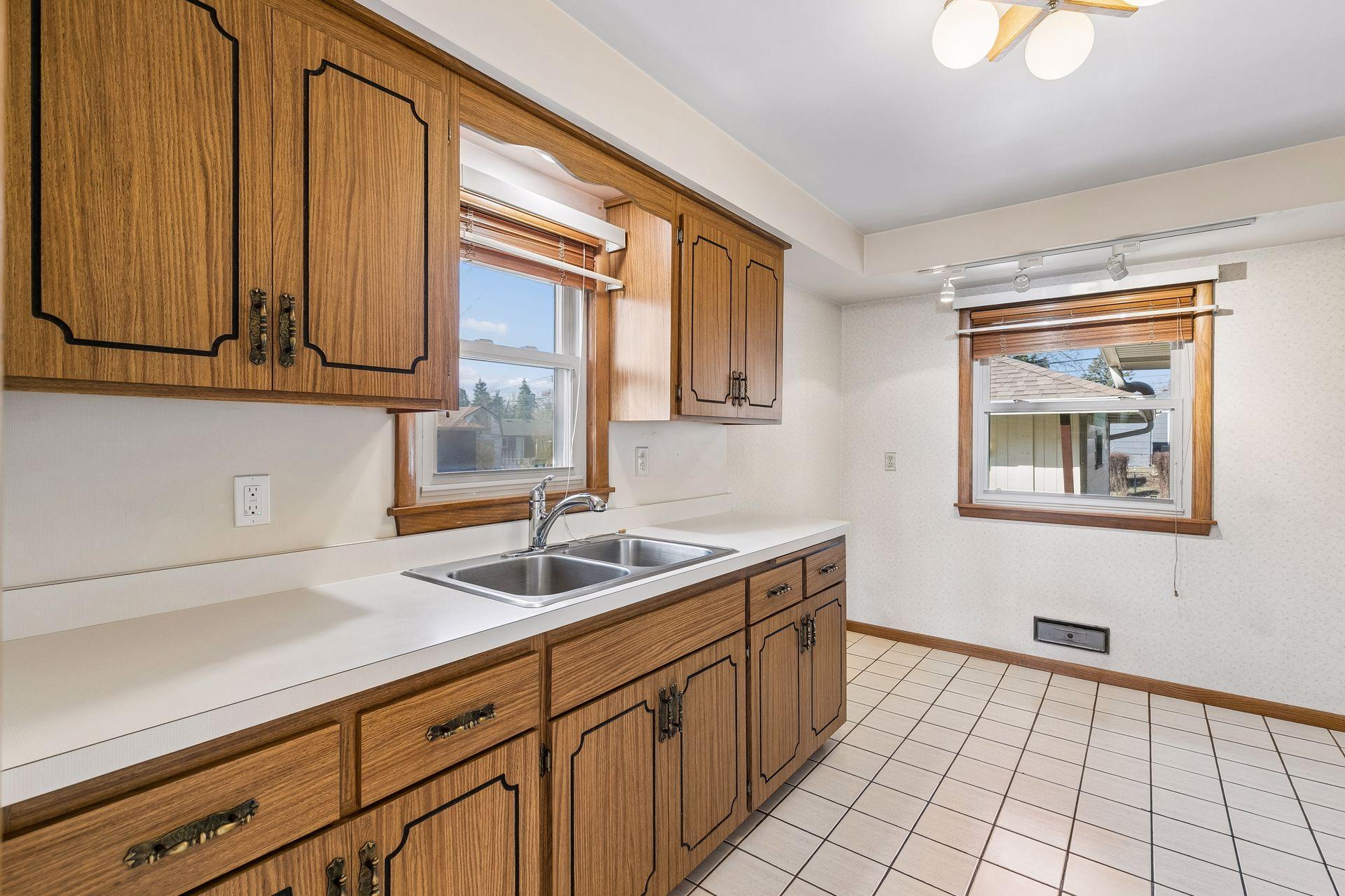 Well appointed kitchen with tile flooring, double sink beneath a window, overhead lighting, and space for casual dining.