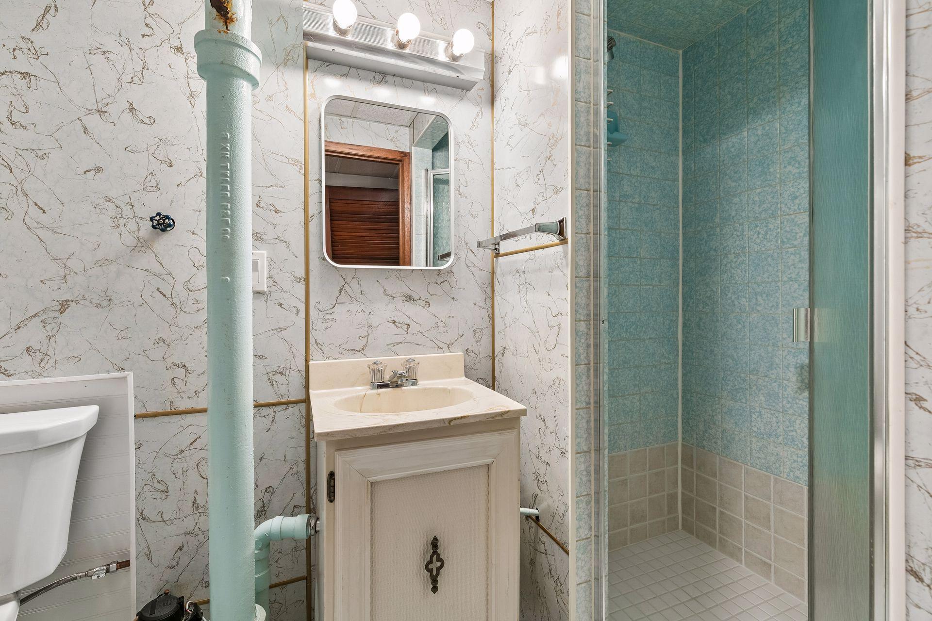 The lower level 3/4 bath features tile floor, a vanity sink, mirror and wall lights, and a full tiled shower.
