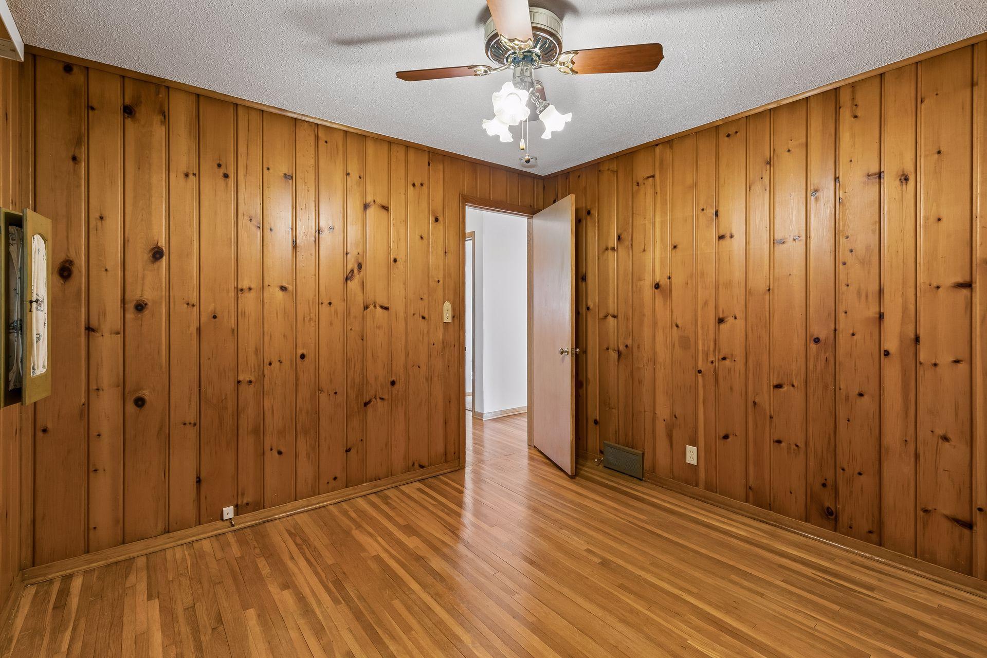 Another main floor bedroom, with warm wood flooring, a ceiling fan, and overhead lighting; perfect for a home office or bedroom. Flexible space can be used as formal dining space.