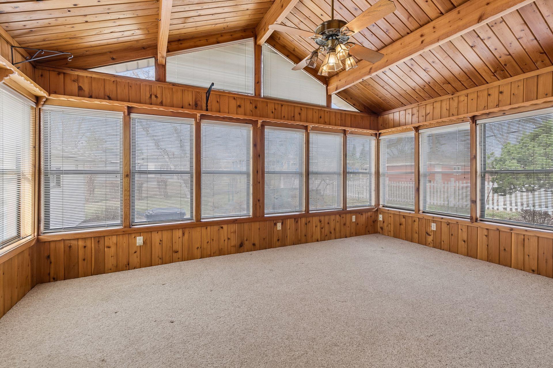 Spacious and airy sunroom with carpet flooring, ceiling fan with overhead lighting, abundant windows, and a wall mounted AC unit.