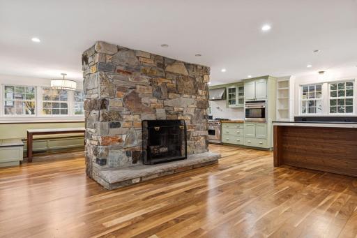 Spacious open-concept room featuring a stunning stone fireplace, hardwood floors, and a modern kitchen with high-end appliances. Perfect for entertaining and family gatherings.
