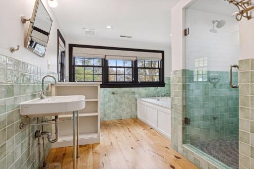 Timeless primary bathroom with elegant green tile, a spacious walk-in shower, and a relaxing soaking tub. Features large windows for natural light and beautiful wood flooring for a warm ambiance