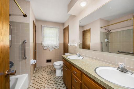 Main floor walk-through full bathroom featuring a double vanity, tile surround tub, and extra storage