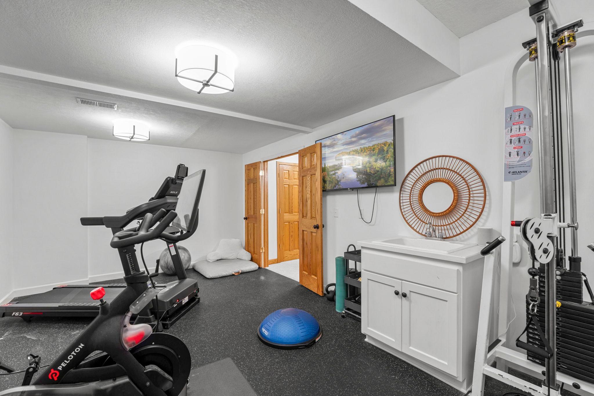 Home gym/bonus room with rubber floor. Cable rack/machine stays. has a sink as well, so this could be a great craft room too!
