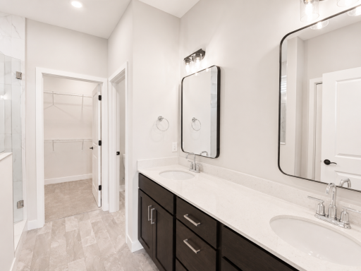 Luxurious owner's bath featuring a dual-sink vanity, quartz countertops, and direct access to the walk-in closet.