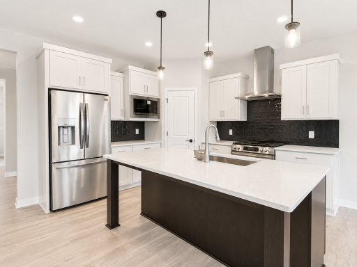 Designer kitchen featuring a large center island, quartz countertops, stainless steel appliances, abundant cabinetry, and a spacious walk-in pantry.