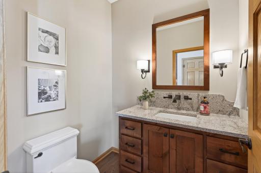 Rustic alder vanity with granite countertop and backsplash, wall-mounted faucet, and continued oak hardwood flooring