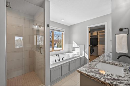 Custom-tiled walk-in shower with frameless glass door, shampoo niche, dual shower heads, full body spray system, and hand shower