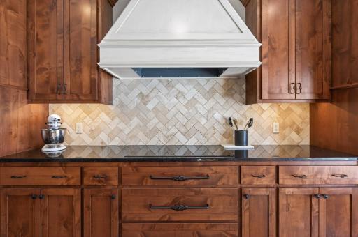 Granite countertops complemented by a natural stone subway tile backsplash, induction cooktop, and cabinet-paneled Vent-A-Hood
