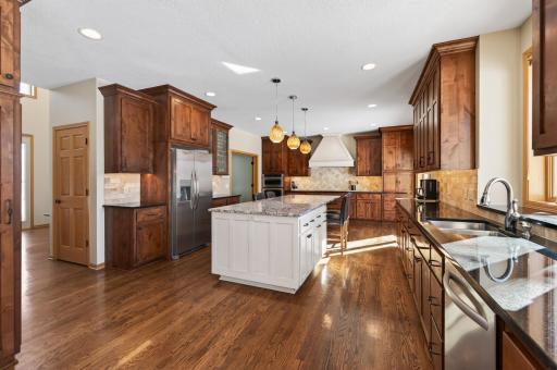 Custom rustic alder cabinetry with raised panel and glass-front doors, under-cabinet lighting, roll-out shelving, and full-height pantry storage