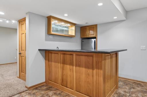 Entertainerâs bar complete with oak cabinetry, glass display doors, roll-out storage, microwave nook, refrigerator, and raised seating counter