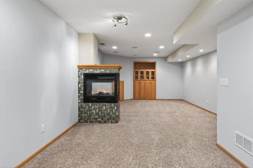 Lower-level family room with custom oak built-in entertainment cabinetry featuring glass doors and open display shelving