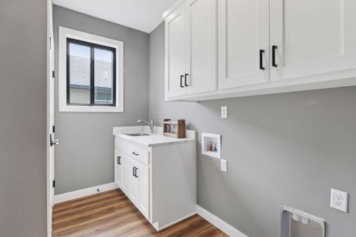 Main floor laundry has upper cabinetry, sink and large closet