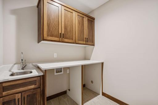 Main floor laundry features upper cabinetry, sink, tile floor