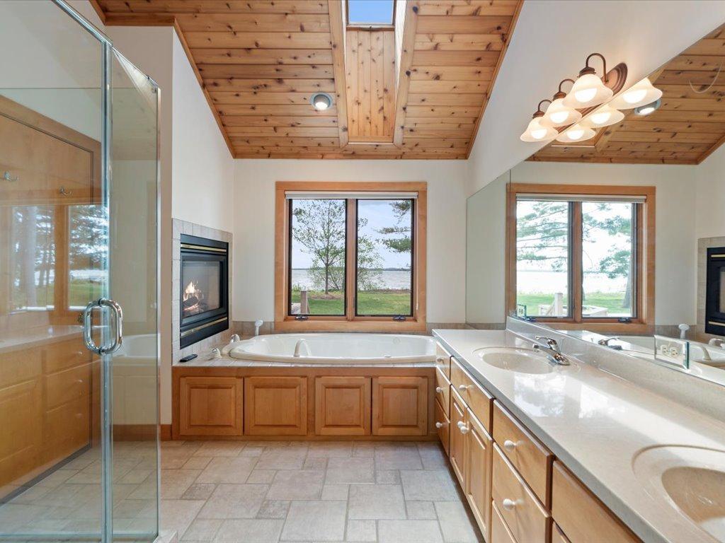 A lakeside soaking tub, fireplace, and serene water views create a private retreat within the primary bath.