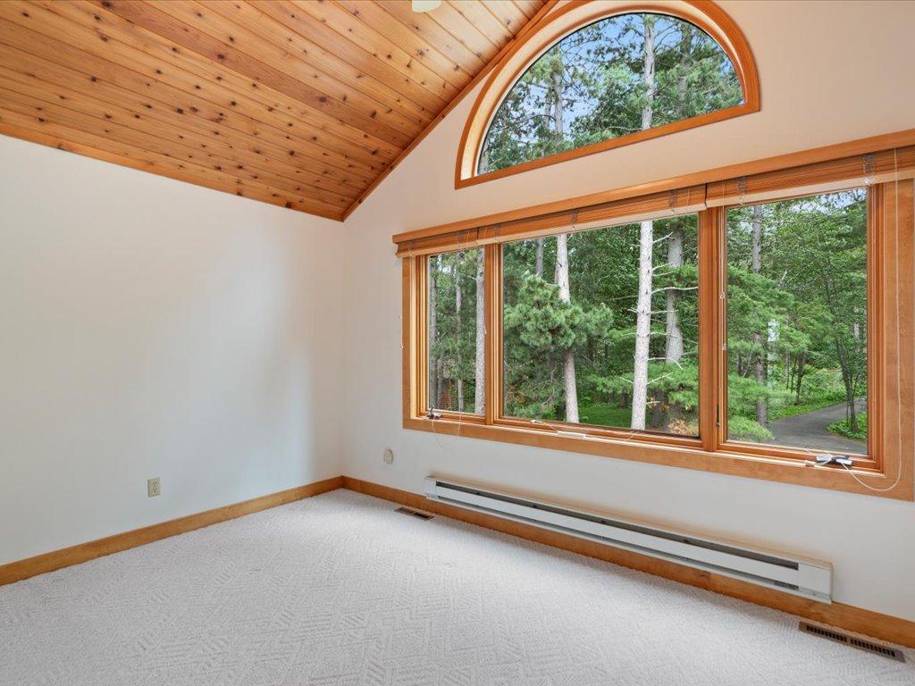 A dramatic arched window and vaulted wood ceiling fill this bedroom with natural light and views of the property's mature pines.