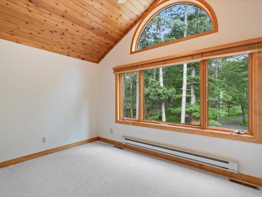 A dramatic arched window and vaulted wood ceiling fill this bedroom with natural light and views of the property's mature pines.
