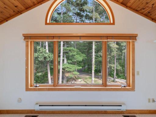 A dramatic arched window and vaulted wood ceiling fill this bedroom with natural light and views of the property's mature pines.