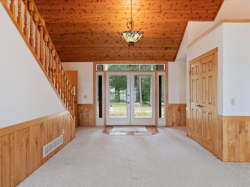 The welcoming foyer features a soaring wood ceiling, elegant staircase, and abundant natural light, creating a warm first impression upon arrival.